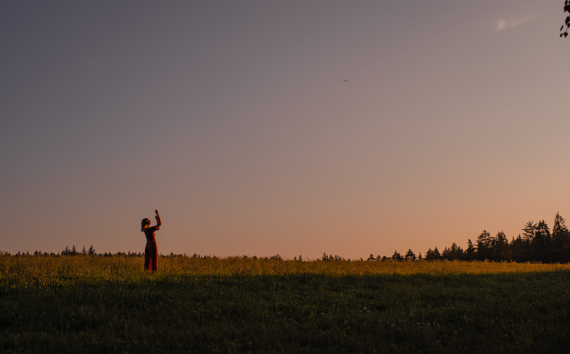 Frau steht im Sonnenuntergang auf dem Feld und hebt die Hände in den Himmel